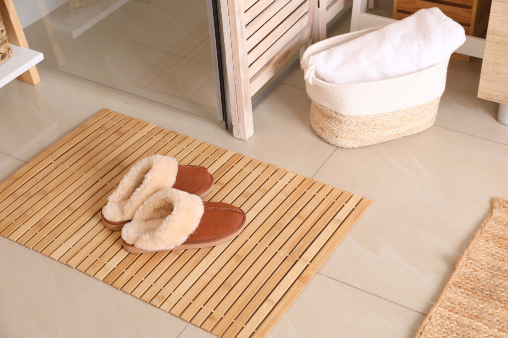 Slippers sit on a bamboo mat outside a shower in a bathroom. The shower also has bamboo doors as part of an eco-friendly bathroom conversion. 